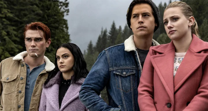 Four young adults stand together in outdoor wooded setting; serious expressions, wearing jackets.