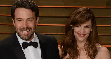 Man in black tuxedo and woman in a silver dress smiling together at an event.