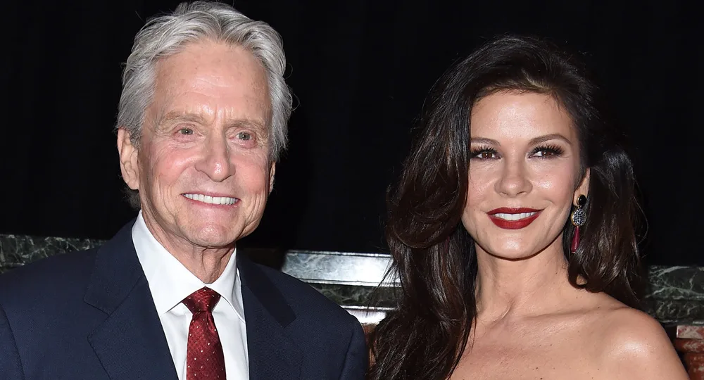 Two people, a man in a dark suit and red tie and a woman with long dark hair, smiling at a formal event.