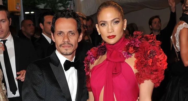 A man in a black suit and bow tie stands beside a woman in a vibrant red floral dress at a formal event.