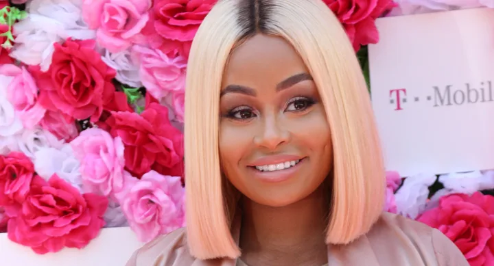 Blonde woman smiling in front of a wall of pink and white flowers, T-Mobile sign partially visible.