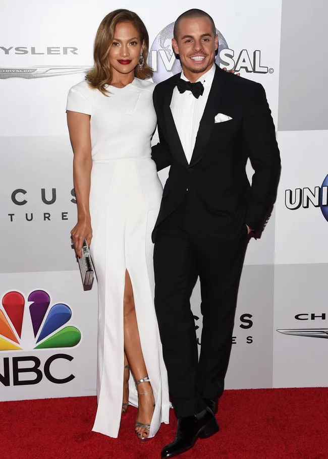 A woman in a white dress and a man in a black tuxedo pose on the red carpet at an event.
