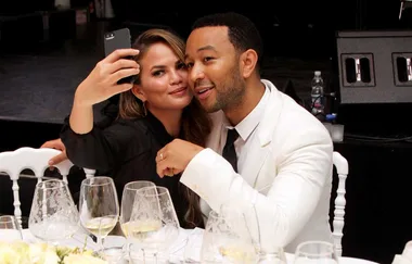 A couple taking a selfie at a formal event, seated at a table with wine glasses.
