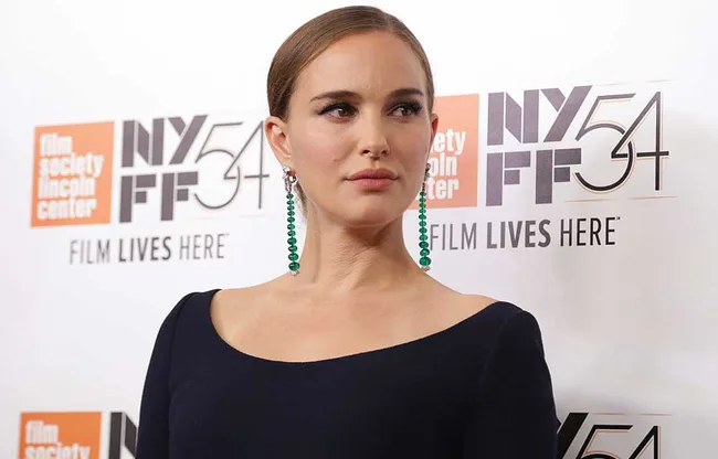 A woman in a black dress with green earrings at NYFF54, Film Society Lincoln Center backdrop.
