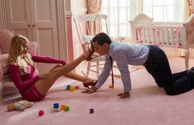 Man in suit crawls towards woman in pink dress sitting on a nursery floor with toys around.