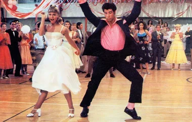 Two people dancing energetically at a lively school dance, surrounded by spectators in colorful outfits.