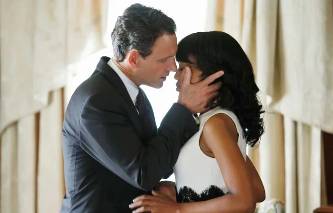 Man in suit and woman in white dress share an intimate moment indoors, close and touching faces.