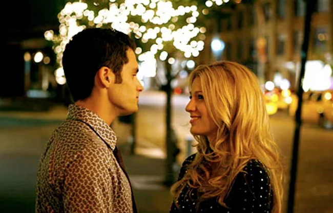 A couple stands facing each other under glowing lights on a city street at night.