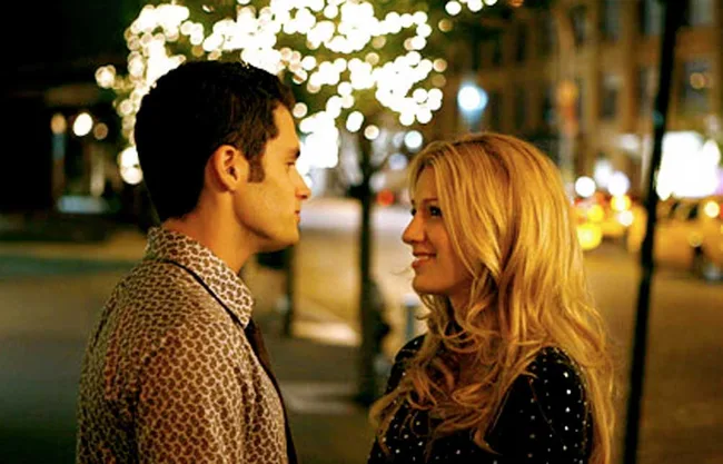 A couple stands facing each other under glowing lights on a city street at night.