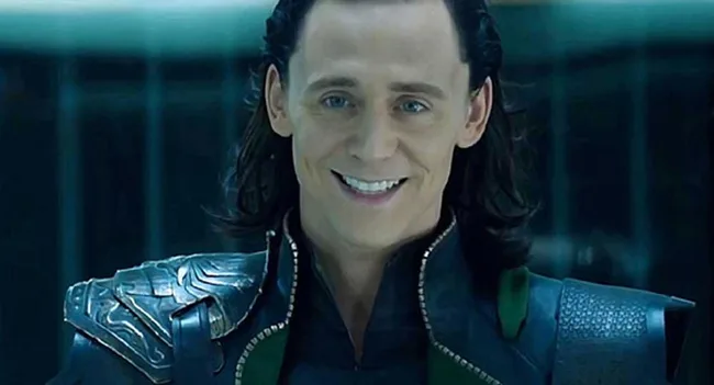 A character in dark armor smiles slightly in a dimly lit room, evoking a mysterious and mischievous aura.