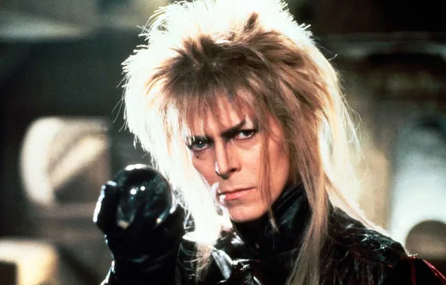 Character with wild hair holding a crystal ball, intense expression, in a fantasy setting.