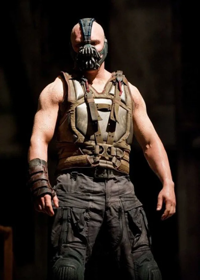 Bane from "The Dark Knight Rises" wearing a mask and a tactical vest, standing confidently in a dimly lit setting.