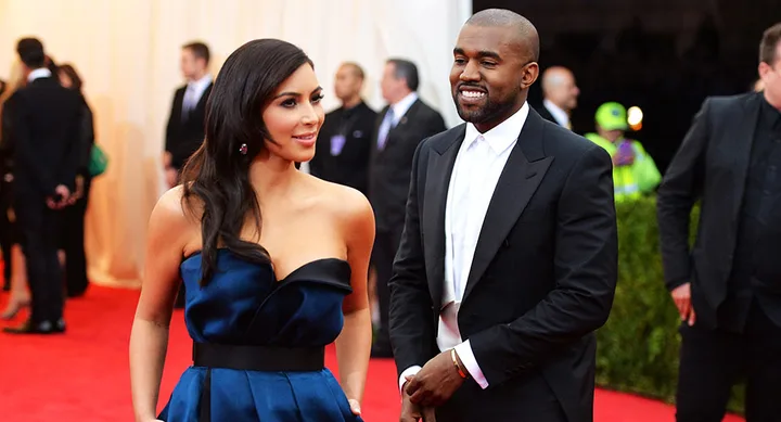 Two well-dressed individuals on a red carpet, with others in the background.