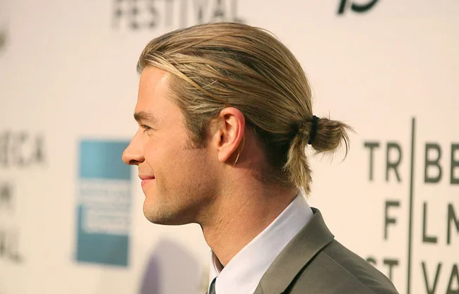 Man with slicked-back hair in a bun, in profile, at a film festival event background.