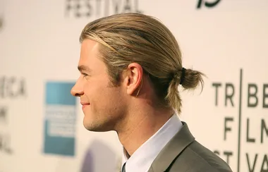 Man with slicked-back hair in a bun, in profile, at a film festival event background.