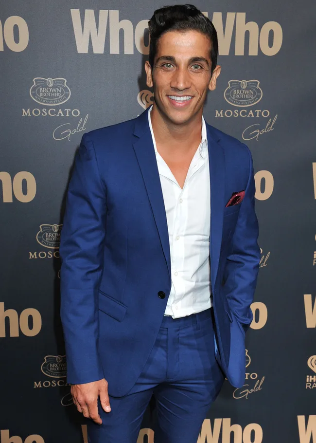 Man in a blue suit smiles at a "Who" magazine event backdrop.