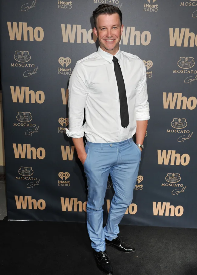 A person in a white shirt and blue pants poses on the red carpet at a "Who" magazine event.