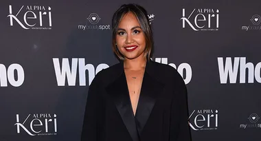 Young woman in black outfit smiles at "Who" event backdrop.