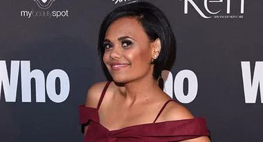 Woman in burgundy dress posing on red carpet with "Who" magazine backdrop.