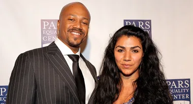 A smiling man in a pinstripe suit and a woman with long dark hair at an event, "PARS Equality Center" backdrop.