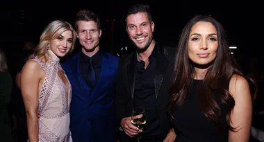 Group of four people smiling and posing at an event, with one holding a glass of wine.