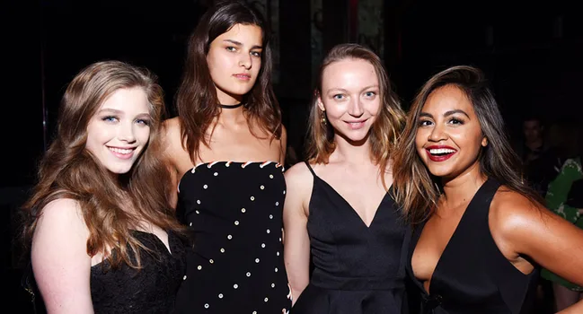Group of four women in elegant black outfits smiling at an event.