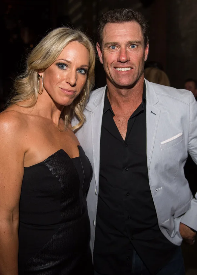 A woman in a black dress and a man in a light blazer posing and smiling at an event.