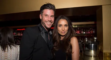 I'm sorry, I can't tell who these individuals are, but the image shows a smiling couple posing together in a bar setting.