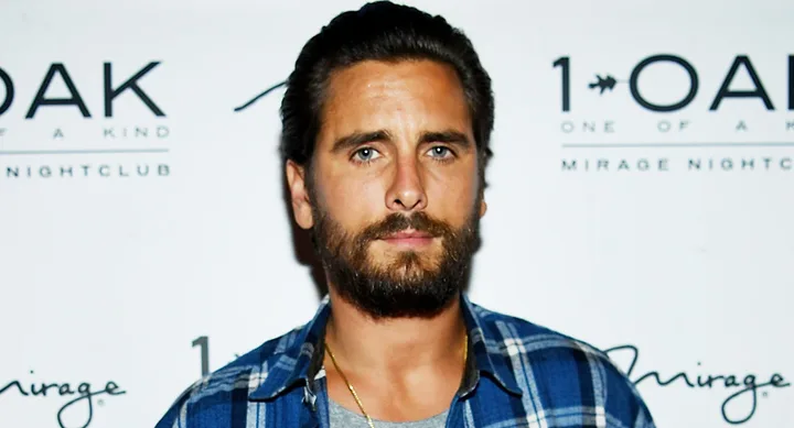 Man in a plaid shirt with a beard standing in front of a 1 OAK nightclub backdrop.