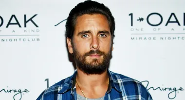 Man in a plaid shirt with a beard standing in front of a 1 OAK nightclub backdrop.