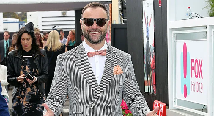 Man in striped suit, peach bow tie, and sunglasses smiling, standing near a Fox hit 101.9 sign.