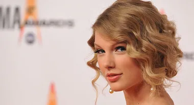 A person with curly hair, wearing pearl earrings, looking over their shoulder at a formal event.
