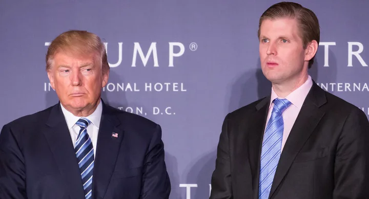 Two men in suits stand in front of a backdrop with "Trump International Hotel" text.