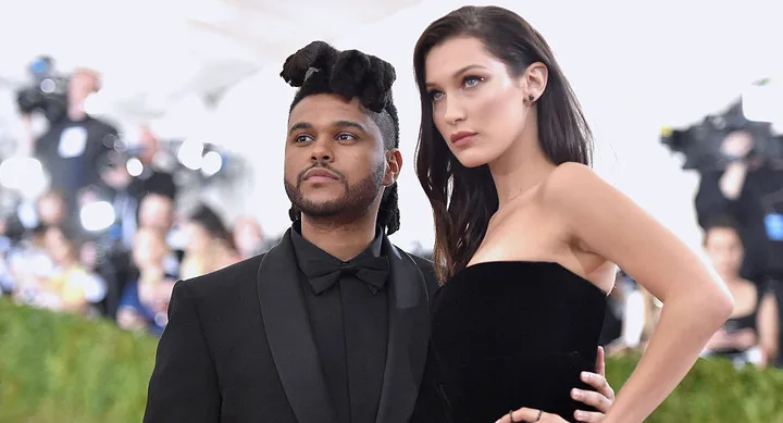 Two individuals in formal attire pose on a red carpet with people and cameras in the background.