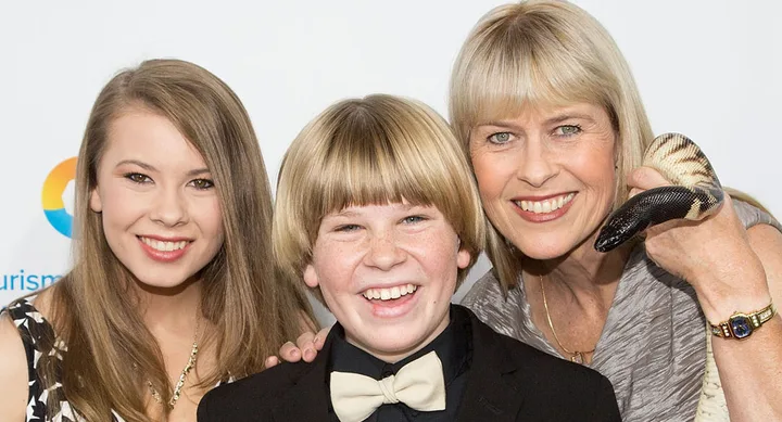 Three people smiling at the camera; one holding a snake.