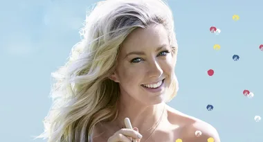 Blonde woman smiling, holding a pen against a light blue background with colorful dots.