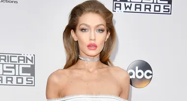 Model wearing a white dress at the American Music Awards, standing in front of a branded backdrop.