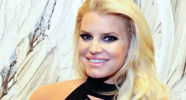 A person with long blonde hair smiles in front of an abstract background.