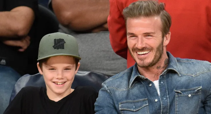 A man and a young boy in a cap smile while seated at a sporting event.