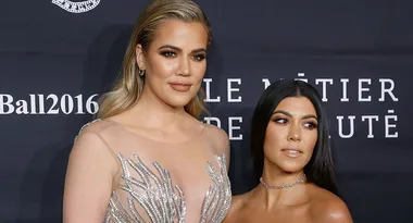 Two women pose on a red carpet, one in a sheer embellished dress, smiling.