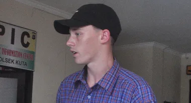 Man in a plaid shirt and black cap standing indoors near an information center sign.