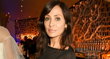 Woman with long brown hair in a black top at an elegant indoor event with warm lighting.