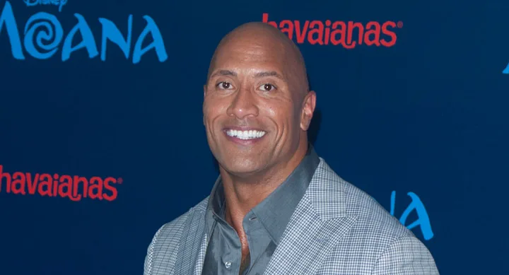 ```
Man smiling at the "Moana" movie event, with a blue background featuring logos.
```