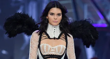Model in lace lingerie with black feathered wings on a fashion runway.