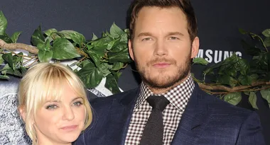 A man in a suit and a woman with blonde hair smiling at a movie premiere with greenery in the background.