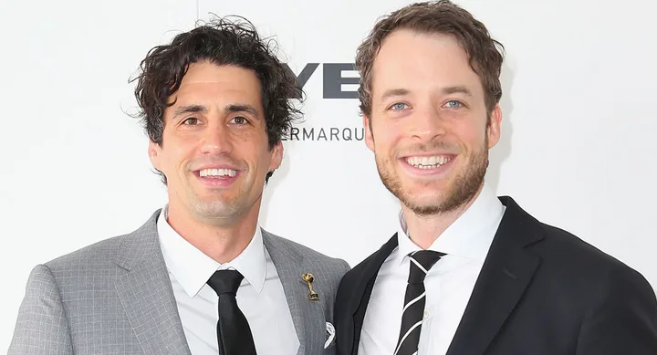 Two smiling men in suits, posing together against a light background at a formal event.
