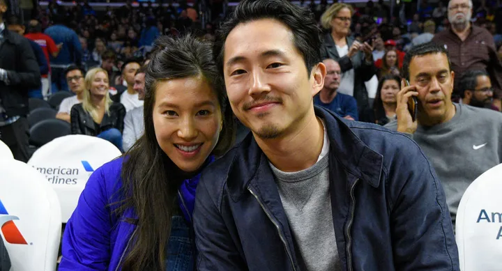 A couple smiling at a sports event, seated with people in the background.
