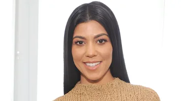 A person smiling in a beige knit top with long black hair against a white background.