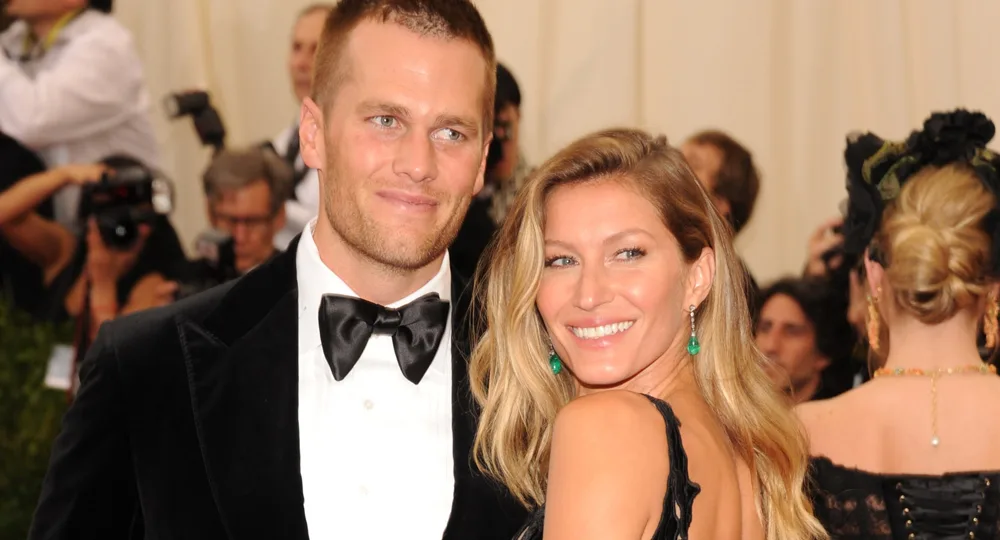 A couple dressed formally, smiling at an event with photographers in the background.