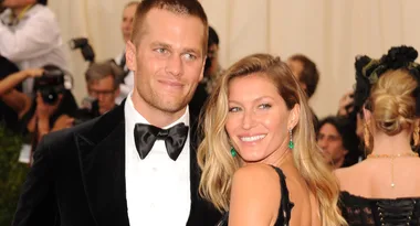 A couple dressed formally, smiling at an event with photographers in the background.